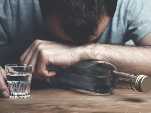 Mężczyzna z butelką alkoholu i kieliszkiem. Nadmierne spożycie alkoholu wpływa negatywnie na lipidogram.