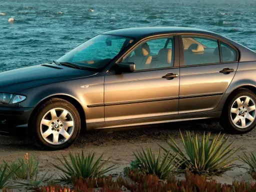 Szary sedan BMW E4 na plaży, z morzem w tle.