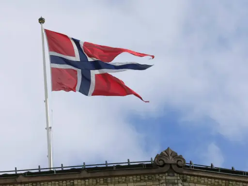 Norwegische Flagge weht im Wind über einem Gebäude. Die Diskussion über den Stromverbrauch in Norwegen ist aktuell.