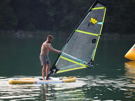 Mężczyzna na desce z żaglem, gotowy do wind sup. Na żaglu pszczółka i napis "3.5".
