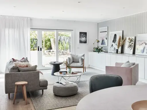 Elegante salón con sofás grises y rosas, mesa de centro y **cuadros apoyados en muebles** de la pared.