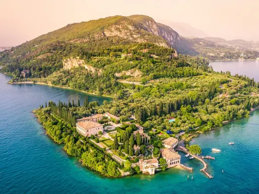 Punta San Vigilio: eine Villa mit Gärten und Zypressen am türkisfarbenen Gardasee, umgeben von grünen Hügeln.