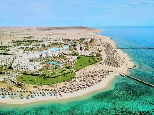 Albatros Palace Port Ghalib: rozległy kompleks hotelowy z basenami, palmami i plażą pełną leżaków, otoczony pustynnym krajobrazem i turkusowym morzem.