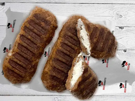 Gegrillte Bifteki, eines davon aufgeschnitten, zeigt eine cremige Füllung. Perfekt, um Bifteki selber machen zu lernen!