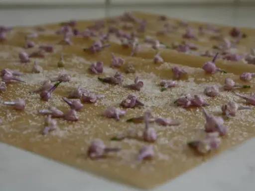 Små, lila syrenblommor strös med socker på ett bakplåtspapper. Kanderade syrenblommor som väntar på att torka.