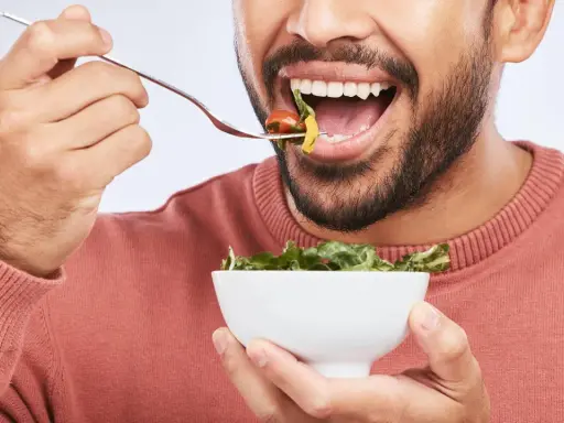 Mann isst Salat, achtet auf die richtige Anzahl, wie oft kauen, für eine gute Verdauung.