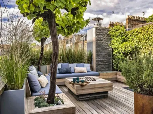 Un coin salon confortable pour aménager une terrasse avec des coussins bleus, une table basse en bois et une végétation luxuriante.