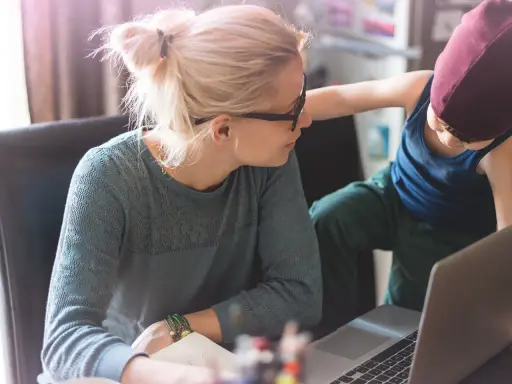 Une mère travaille sur son ordinateur portable, son enfant curieux s'approche. Un moment de vie quotidienne illustrant l'équilibre digital.