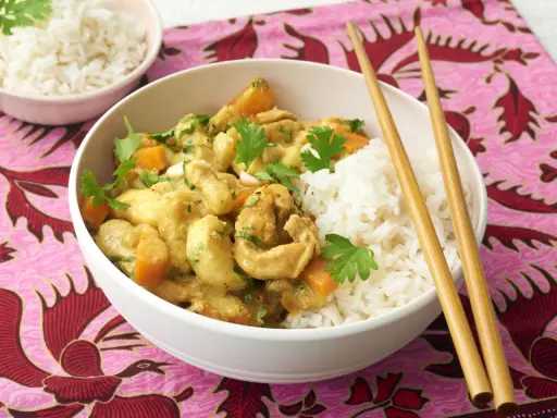 Ein köstliches Bananencurry mit Hähnchen, Karotten und Reis, garniert mit Koriander. Chopsticks liegen bereit.