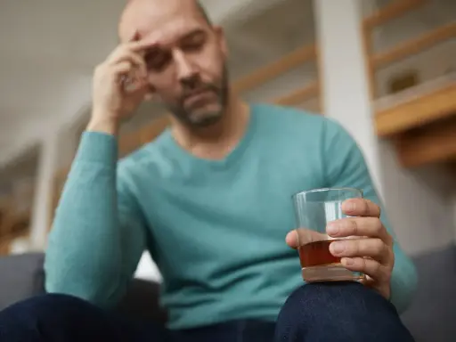 Mężczyzna z bólem głowy trzyma szklankę alkoholu, być może doświadczając reakcji disulfiramowej objawy.