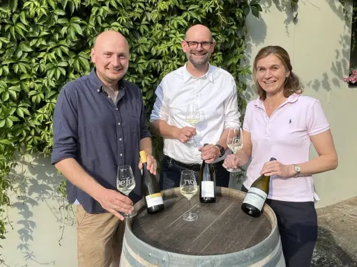 Drei Personen präsentieren Wein. Die Flasche mit Auxerrois Aussprache ist im Fokus.