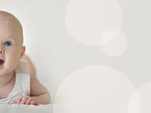 Uśmiechnięte niemowlę 4 miesiące leży na brzuchu, z otwartymi ustami i szeroko otwartymi oczami, patrząc wprost na widza.