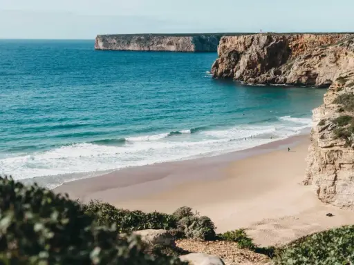 Ein einsamer Surfer genießt die Wellen am Sagres Strand, umgeben von steilen Klippen und dem weiten Atlantik.