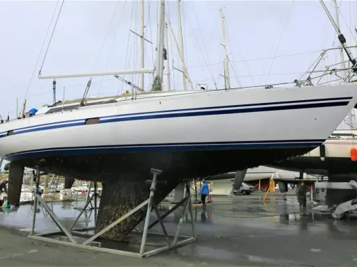Un grand voilier blanc et bleu est sur des chandelles, son flanc couvert de bernacles. Un homme nettoie la coque d'un autre bateau à proximité.