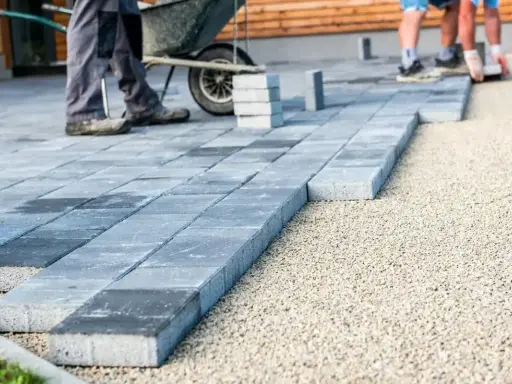 Układanie betonowych płyt na żwirze. Pracownicy tworzą ścieżkę, gdzie beton zamiast kostki staje się nowoczesnym rozwiązaniem.