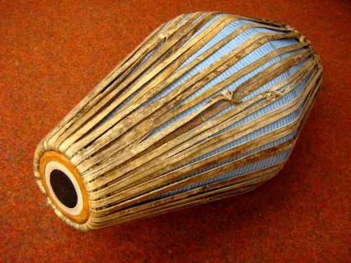 Mridanga, jeden z najstarszych instrumentów muzycznych, z niebieską membraną i drewnianymi wzmocnieniami, leży na pomarańczowym tle.