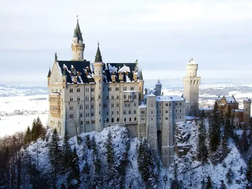 Zamek Neuschwanstein w zimowej scenerii, otoczony ośnieżonymi drzewami i krajobrazem.