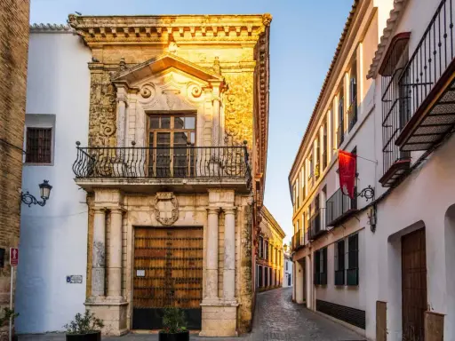 Calle empedrada flanqueada por edificios históricos, un ejemplo de los pueblos bonitos de Sevilla. Fachada de piedra dorada con balcón y puerta de madera.