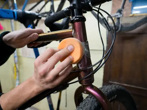 Hände polieren den Fahrradrahmen mit einem orangen Schwamm, um den Fahrradlack auszubessern.