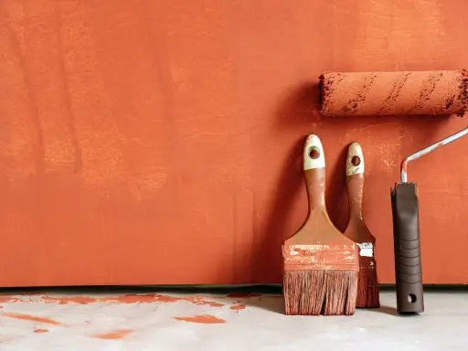 Deux pinceaux et un rouleau à peinture, prêts à rattraper trace de rouleau peinture sur un mur orange texturé.