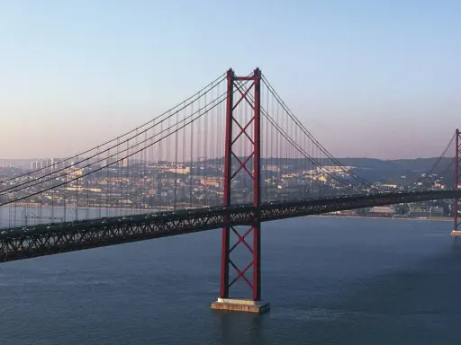 Der rote Hängebrücken-Gigant, oft als "Golden Gate Lissabon" bezeichnet, überspannt das ruhige Wasser mit der Stadt im Hintergrund.