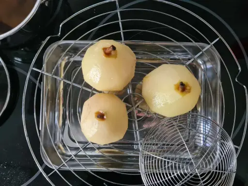 Trois poires pochées, prêtes pour une délicieuse recette tarte bourdaloue, égouttent sur une grille.
