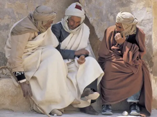 Drei Männer in traditioneller Kleidung sitzen und unterhalten sich. Sie diskutieren vielleicht, was haben Araber erfunden, während sie die Sonne genießen.