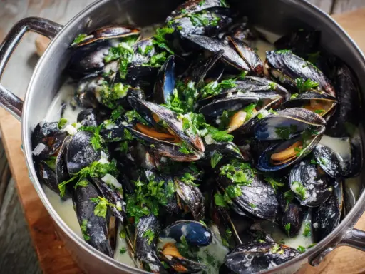 En stor gryta med ångande moules marinières, toppad med färsk persilja och serverad i en krämig vitvinssås.
