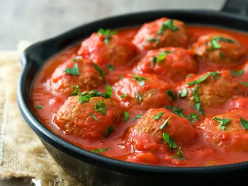 Polpette di carne succulente in salsa di pomodoro, guarnite con prezzemolo fresco, servite in una padella di ghisa.