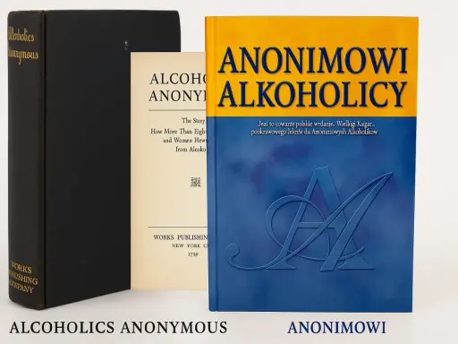 Trzy książki: czarna z napisem "Alcoholics Anonymous", kremowa z tekstem "Alcoholics Anonymous" i niebiesko-żółta z tytułem "Anonimowi Alkoholicy".