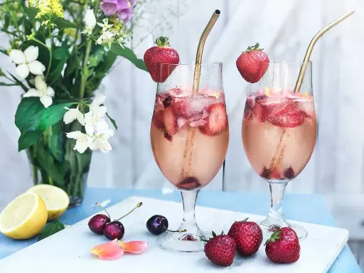 Två glas med drink med gin och prosecco, fyllda med is, jordgubbar och körsbär. Garnerade med jordgubbar och serverade med blommor och citron.