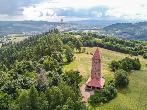 Kamienna wieża widokowa na wzgórzu, otoczona lasami i polami. Jedna z wielu wież widokowych na Dolnym Śląsku, oferująca malownicze krajobrazy.