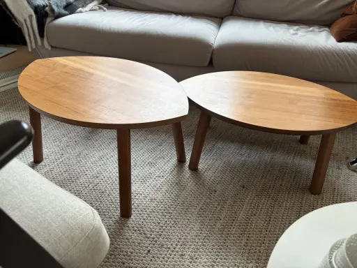 Två ovala soffbord i trä, liknande IKEA:s soffbord i Stockholm, står på en matta framför en soffa.