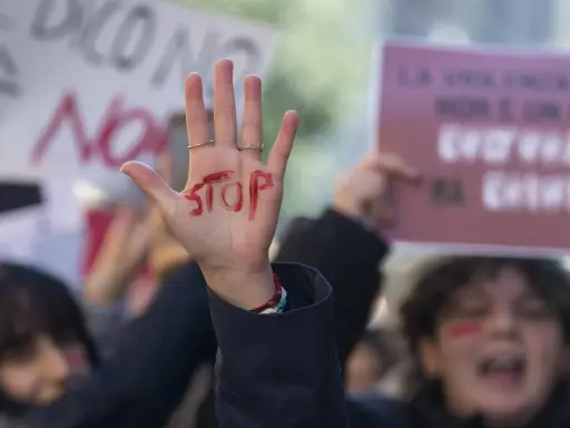 Mano alzata con "STOP" scritto in rosso, simbolo di protesta. Si evoca la necessità di una **codice rosso procedura** per proteggere le vittime.