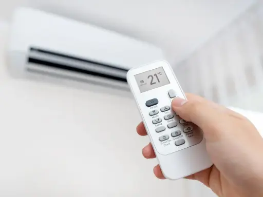 Mano ajustando el control remoto del aire acondicionado a 21°C, modo "Cooling". ¡Así se logra un ambiente fresco y agradable!
