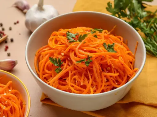 Aksamitna marchewka po koreańsku, udekorowana natką pietruszki, obok czosnku i kolorowego pieprzu.