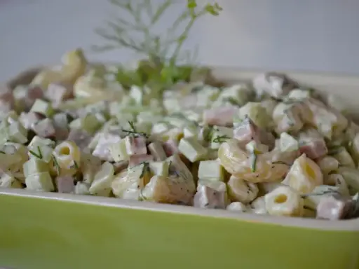 Pyszna sałatka z makaronem, szynką, ogórkiem i serem, udekorowana świeżym koperkiem.