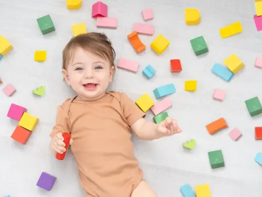 Uśmiechnięte dziecko wśród kolorowych klocków. Czas na zabawę i naukę, jak odpieluchować dziecko.