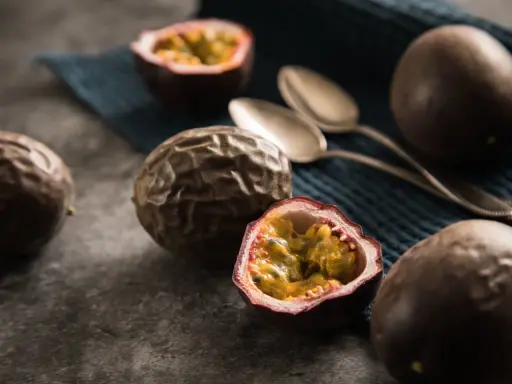 Reife Passionsfrüchte, eine aufgeschnitten, zeigen ihr saftiges Inneres. Zwei Löffel liegen bereit, um die exotische Frucht zu genießen.