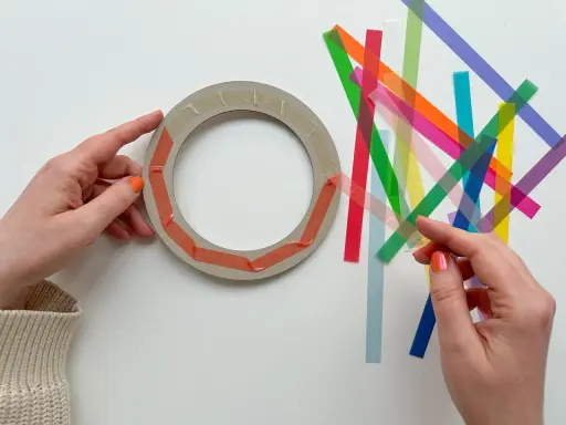 Hände bereiten einen Ring für Fenstersterne vor, indem sie bunte Streifen zum Falten bereitlegen.