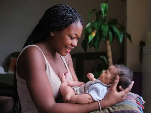 Eine junge Frau hält ihr Baby liebevoll im Arm. Die Frage "wie lange kann man stillen" beschäftigt viele Mütter.
