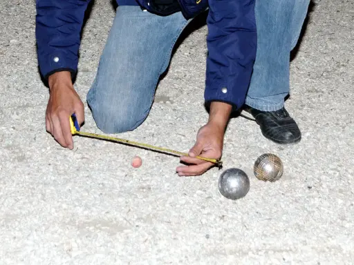Un joueur de pétanque mesure la distance entre les boules. On se demande combien gagne un joueur de pétanque professionnel.