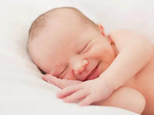 Un bebé duerme plácidamente, con una sonrisa que nos hace preguntar porque sonrien los bebes. Su carita refleja paz y felicidad.