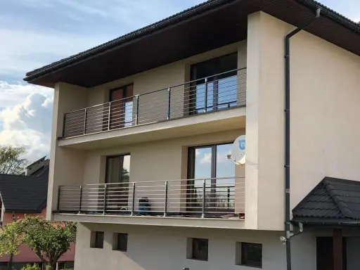 Nowoczesny dom z dwoma balkonami, gdzie zamiast tradycyjnej balustrady zastosowano elegancki murek z poziomymi stalowymi elementami.