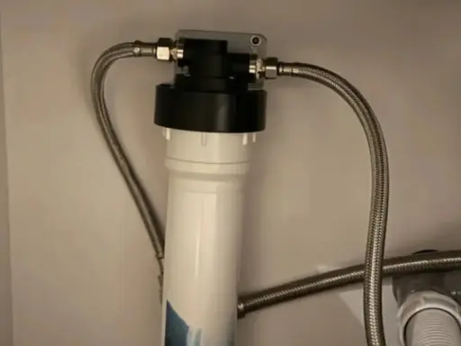 Système de filtration d'eau sous évier avec un cartouche charbon actif blanc et noir, relié par des tuyaux flexibles.