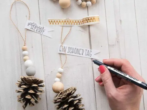 Déco Noël pomme de pin à faire soi-même : des suspensions naturelles avec perles en bois et messages personnalisés.