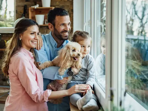 Szczęśliwa rodzina zastępcza, z pieskiem w ramionach, patrzy przez okno. Marzą o adopcji i wspólnym życiu.