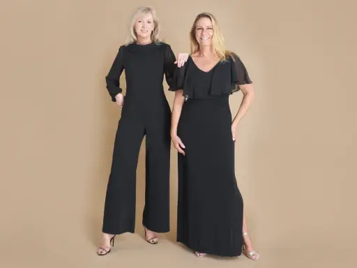 Two women in elegant black evening attire, a wide-leg jumpsuit and a flowing gown, ready for a formal event.