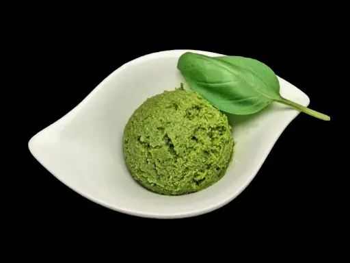 Une cuillère de pesto maison, d'un vert vibrant, garnie d'une feuille de basilic frais, dans une coupelle blanche.