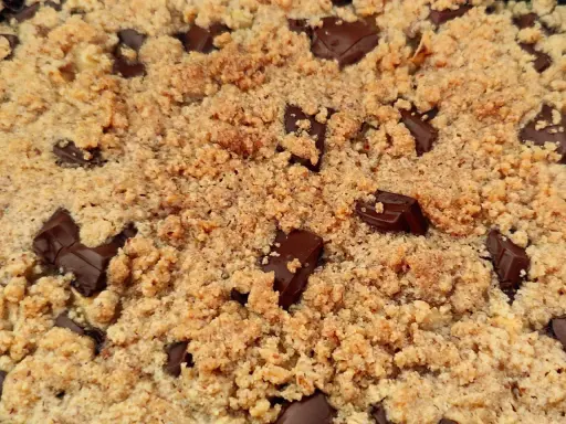 Gros plan sur un délicieux crumble pomme amande parsemé de morceaux de chocolat noir fondants.